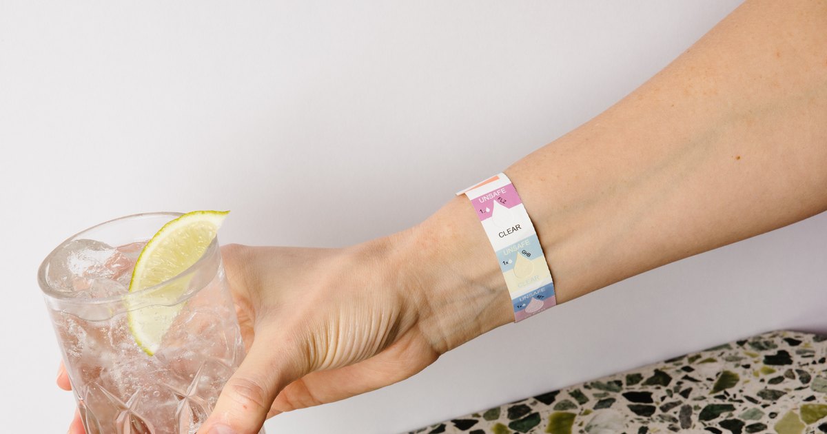 A hand holding a tall glass with a lime wedge, wearing a Verri drink check wristband.